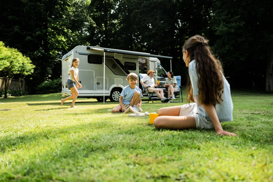 Gezin met kinderen ontspant voor hun camper op een groene camping